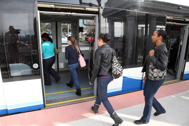 Isang photographic na larawan ng mga pasaherong sumasakay sa isang light rail train sa HRT Tide light rail system.